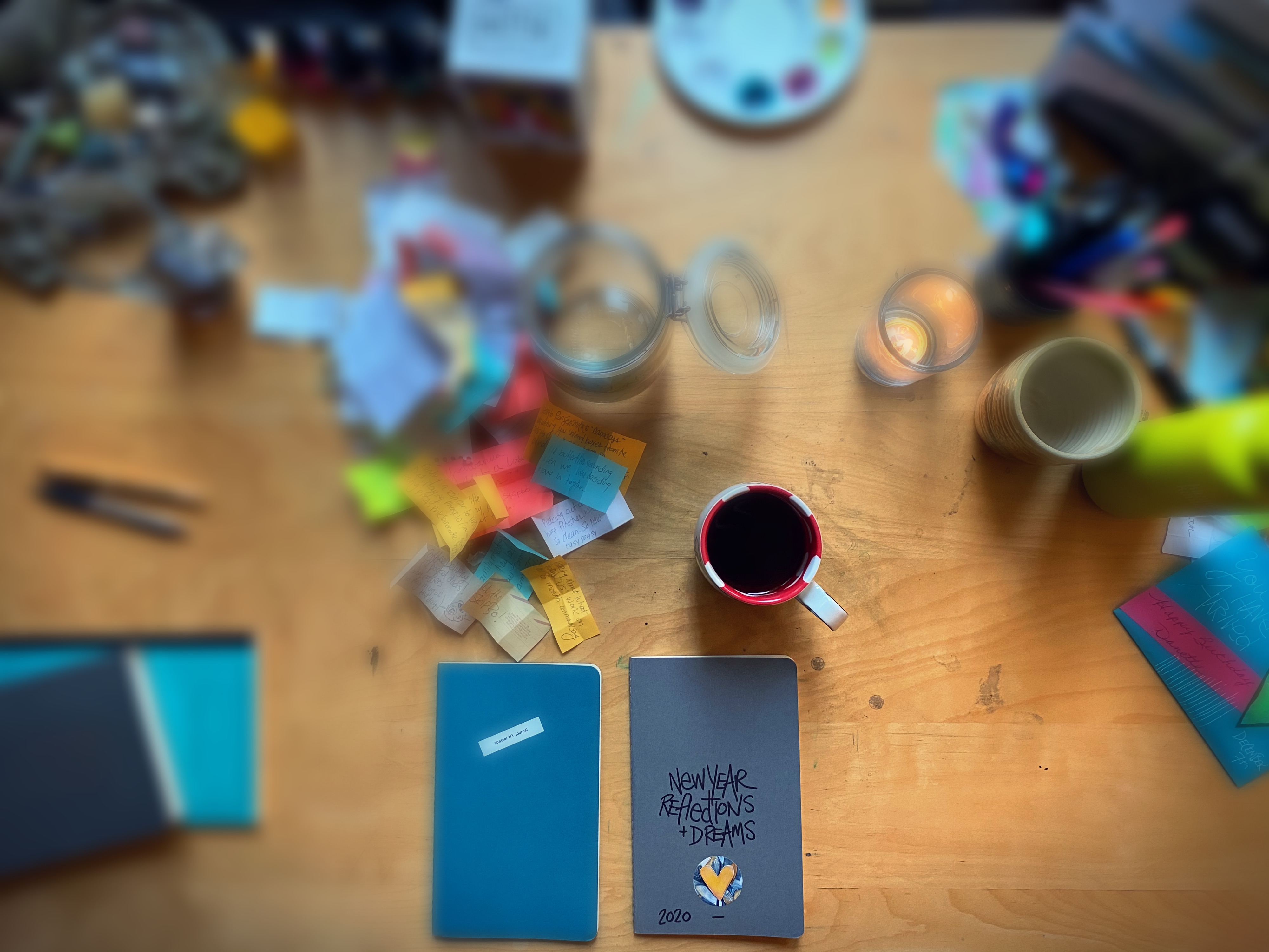 overhead shot of a desk scattered with coloured paper, journals and a coffee