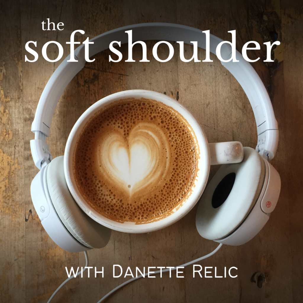 Aerial view of white headphones encircling a latte with a milk foam heart with the lettering "The Soft Shoulder with Danette Relic"