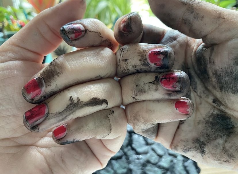 two white hands with chipped nail polish show off black ink stains from making art. 